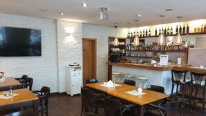 Un restaurante con mesas y sillas de madera, una zona de bar con botellas de vino y un televisor montado en la pared.
