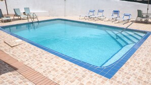 Ein rechteckiger Swimmingpool mit klarem, blauem Wasser, umgeben von beige farbenen Mosaikfliesen.
