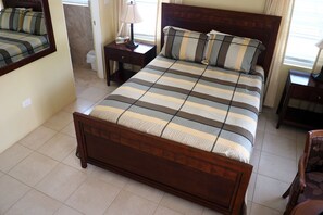 Un dormitorio con cama de madera, mesita de noche, una silla y ventana con cortinas.