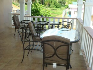 Un patio con una mesa y sillas de vidrio, rodeado de barandillas y columnas blancas.