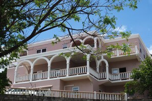 Un edificio de varios pisos con fachada rosa, balcones blancos y un árbol en primer plano.