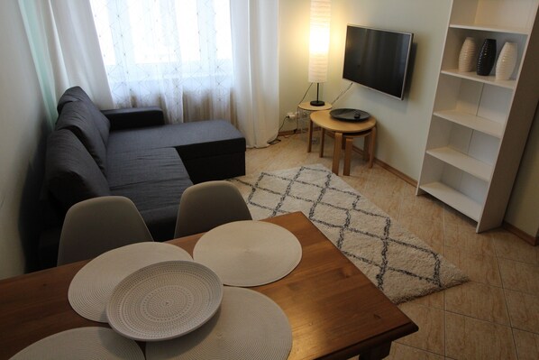 A modern living room with a sofa, a TV, a small table, and a bookshelf.