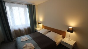 Ein Hotelzimmer mit einem Bett, zwei Nachttischlampen, einem Fenster mit Vorhängen und einem Nachttisch.