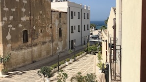 A narrow street with buildings on either side, outdoor seating with tables and chairs, and a view of the sea in the distance. - Egesta (Castellammare del Golfo)