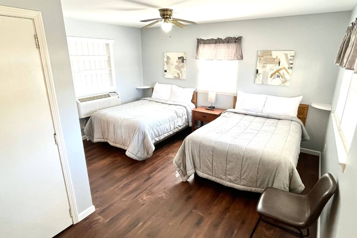 A bedroom with two beds, a ceiling fan, a radiator, and artwork on the walls.