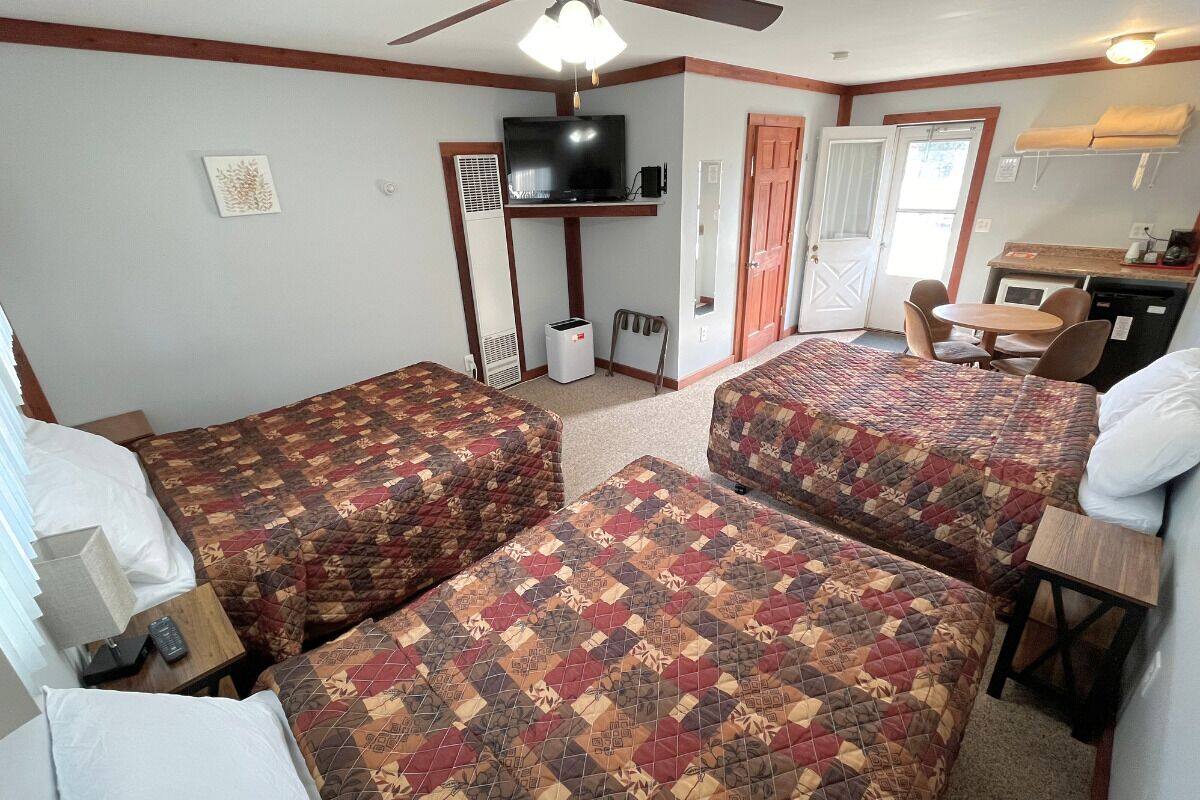 A room with two beds, a TV, a small kitchenette, and a door leading to another room.