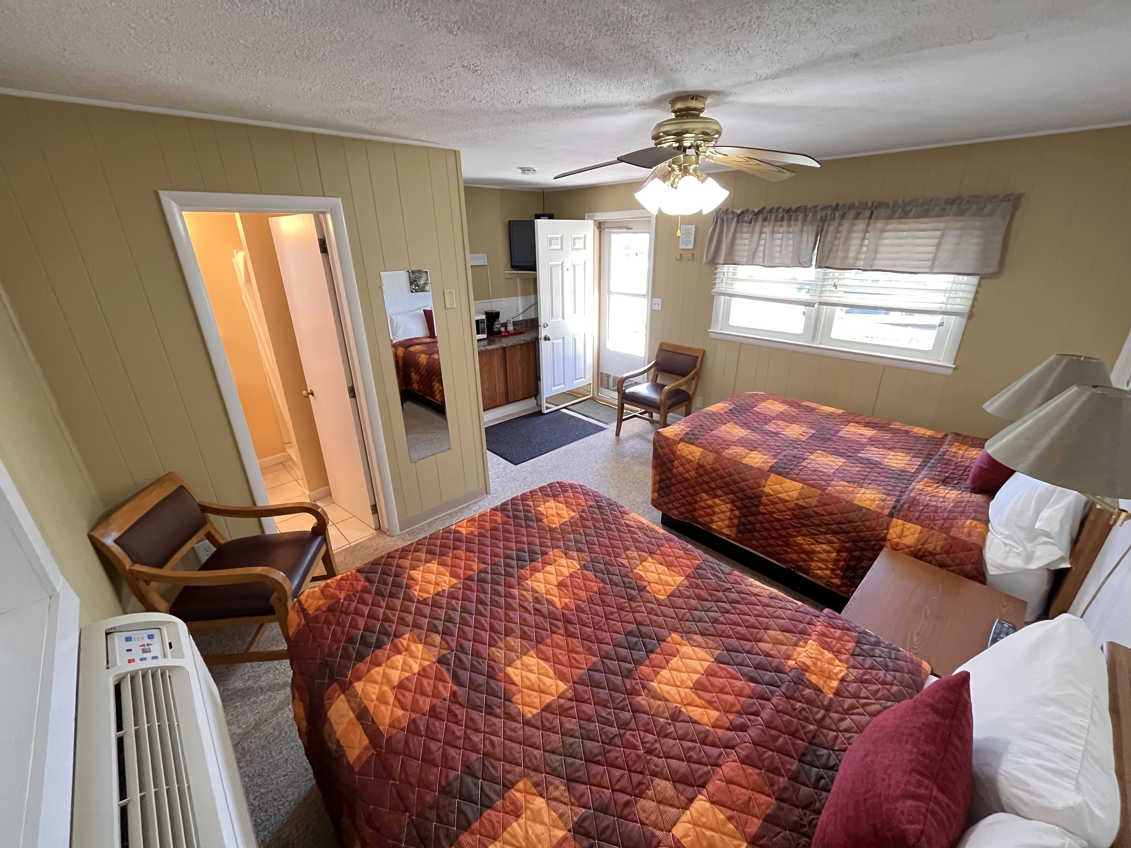 A hotel room with two beds, a ceiling fan, a desk, a chair, and a window with blinds.