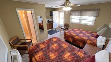 A hotel room with two beds, a ceiling fan, a desk, a chair, and a window with blinds.