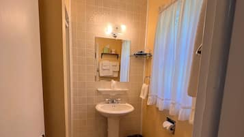 A compact bathroom with a pedestal sink, toilet, and a small trash bin.