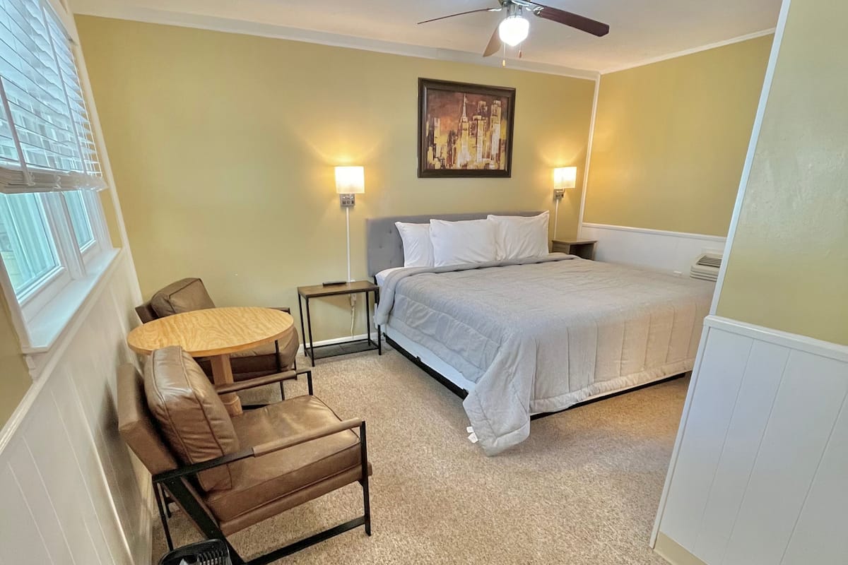 A bedroom with a bed, a chair, a table, and a ceiling fan.