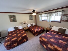 Quarto de hotel com duas camas, ventilador de teto, janela com cortinas e ar-condicionado fixado na parede.