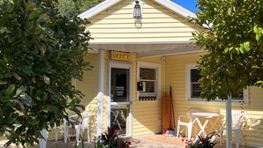 Un bâtiment jaune avec une enseigne indiquant « BUREAU OUVERT » et un petit porche avec des chaises blanches.