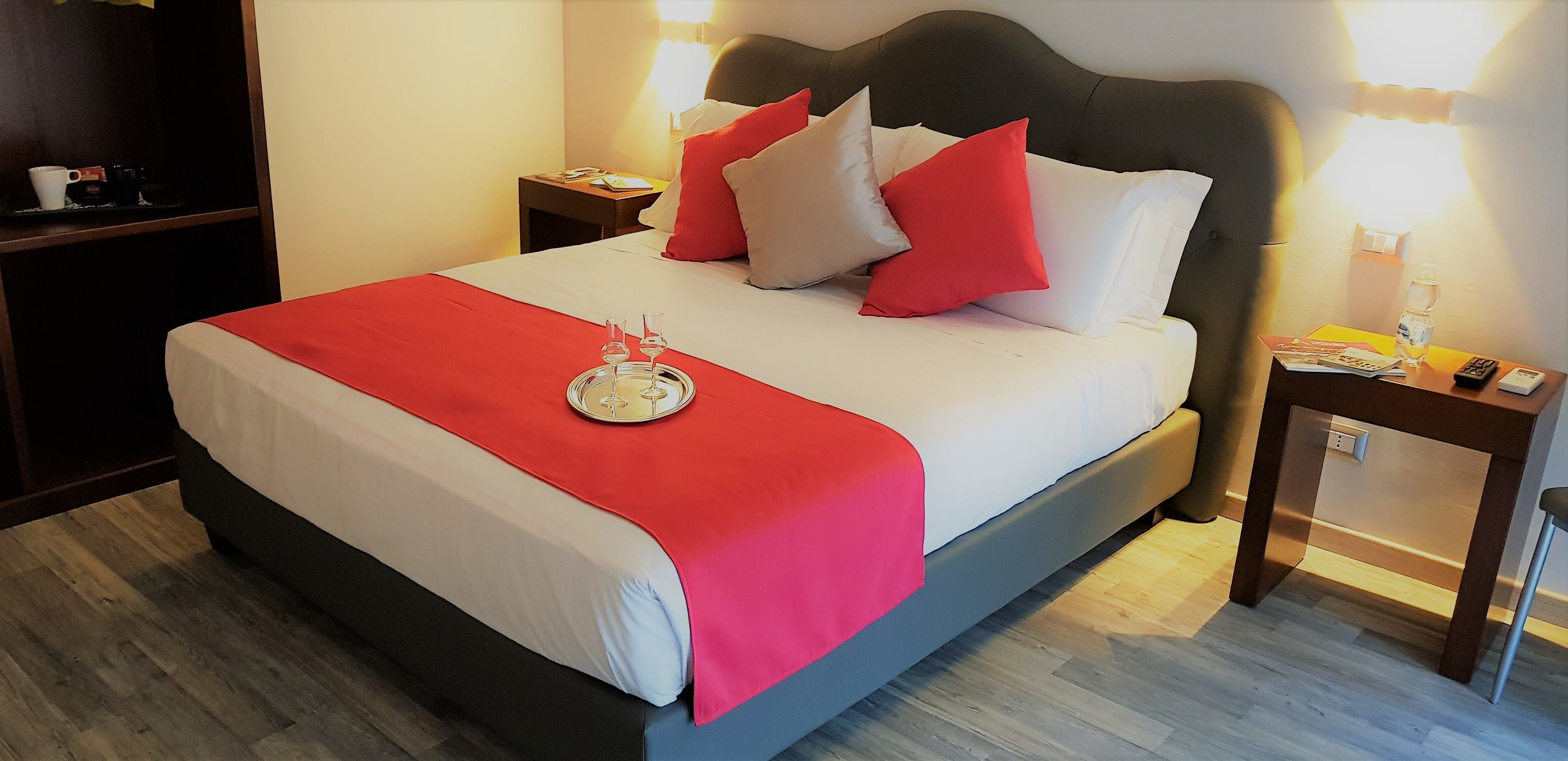 Een hotelkamer met een bed, nachtkastje, lamp, afstandsbediening en een fles water.