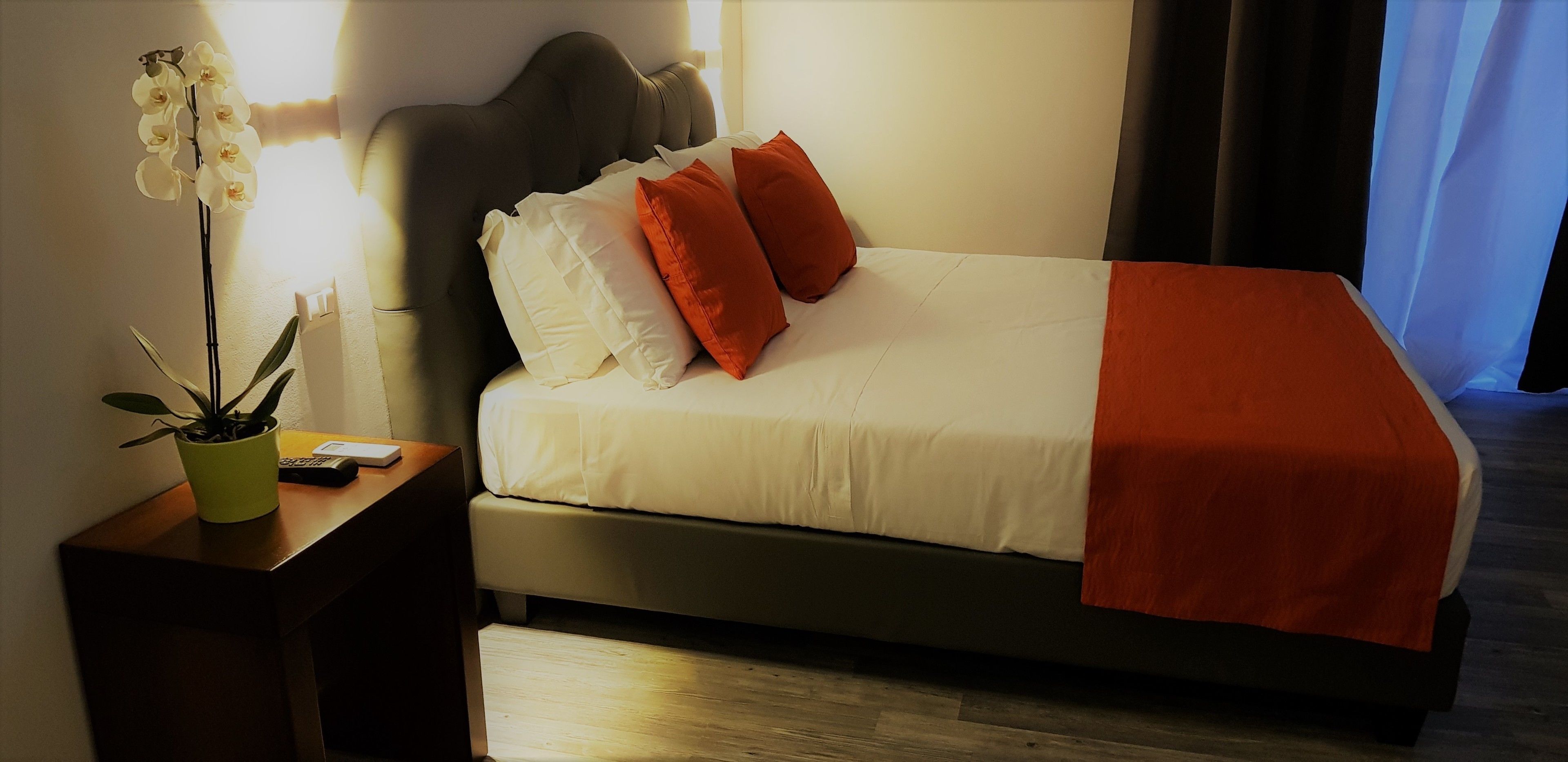 Una habitación de hotel con una cama, una mesita de noche con una planta en maceta y una ventana con cortinas.