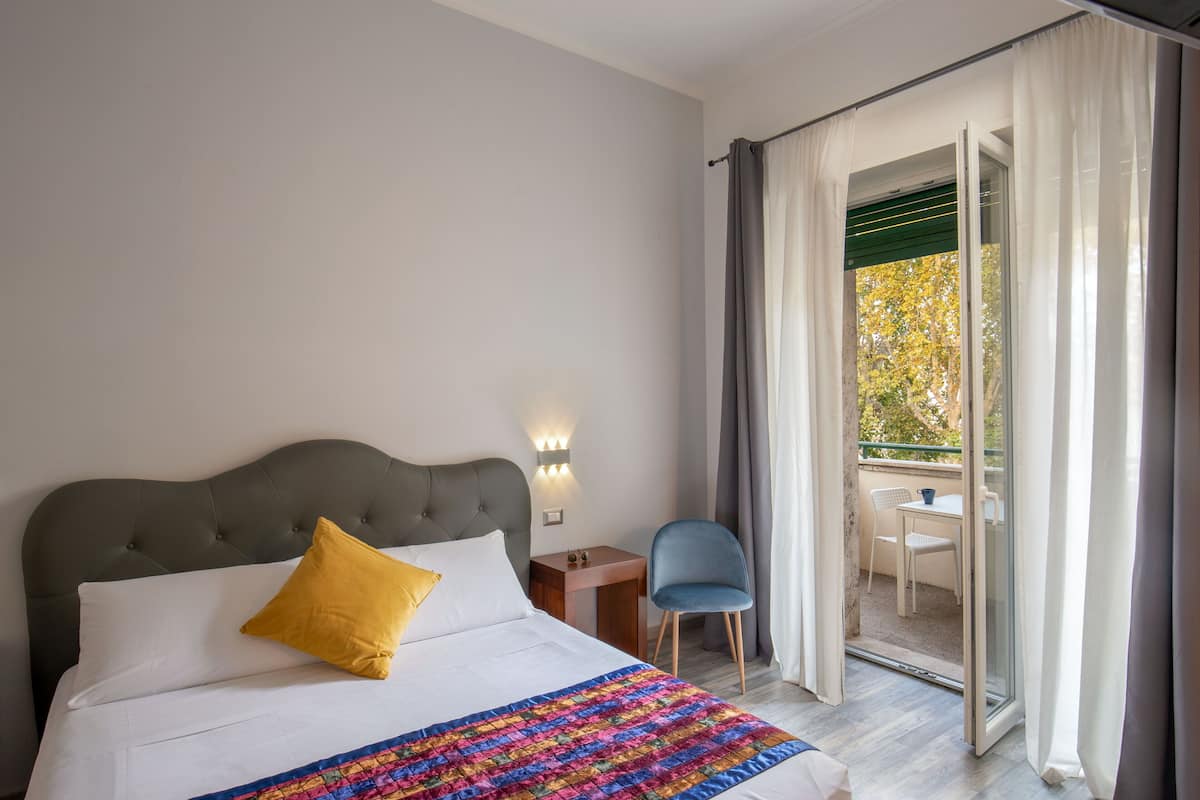 A hotel room with a bed, a nightstand, a chair, and a balcony with a table and chairs.