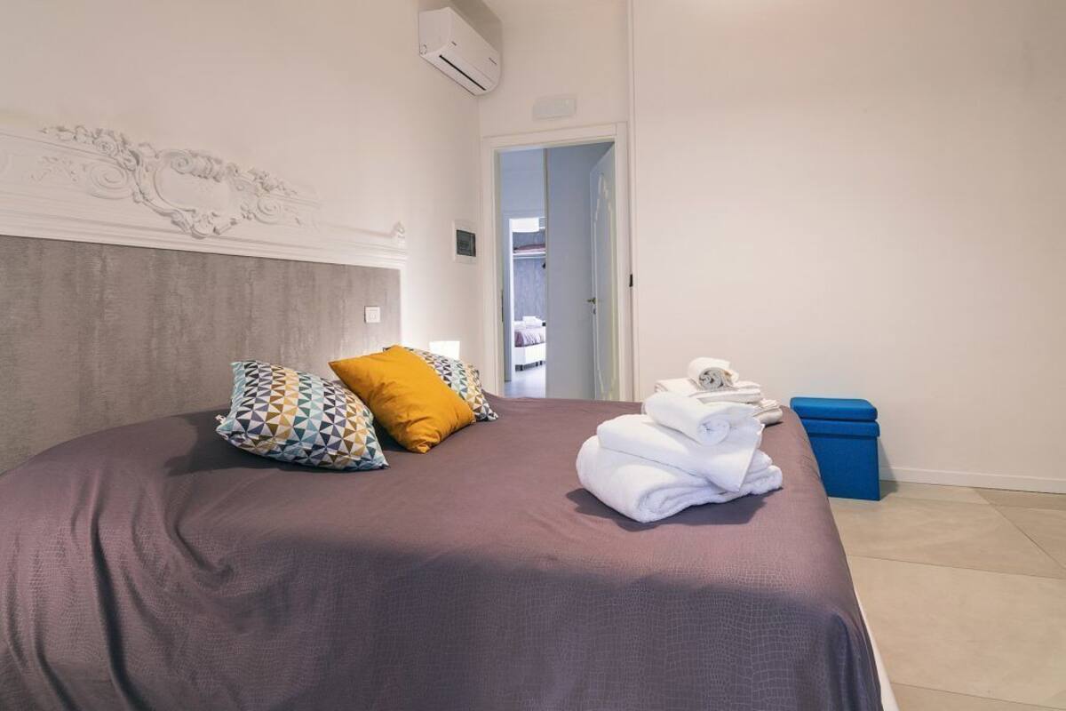 Un letto rifatto con una coperta viola, due cuscini decorati e un asciugamano piegato su un lato.