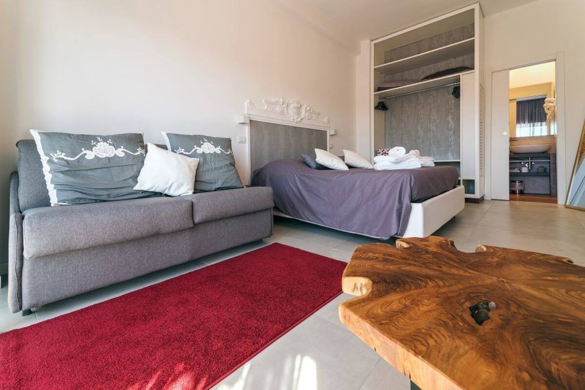 Una camera da letto moderna con un divano grigio, un letto con copriletto viola, un tappeto rosso e un tavolino da caffè in legno.