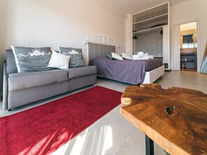 Un dormitorio moderno con un sofá gris, una cama con colcha morada, una alfombra roja y una mesa de centro de madera.