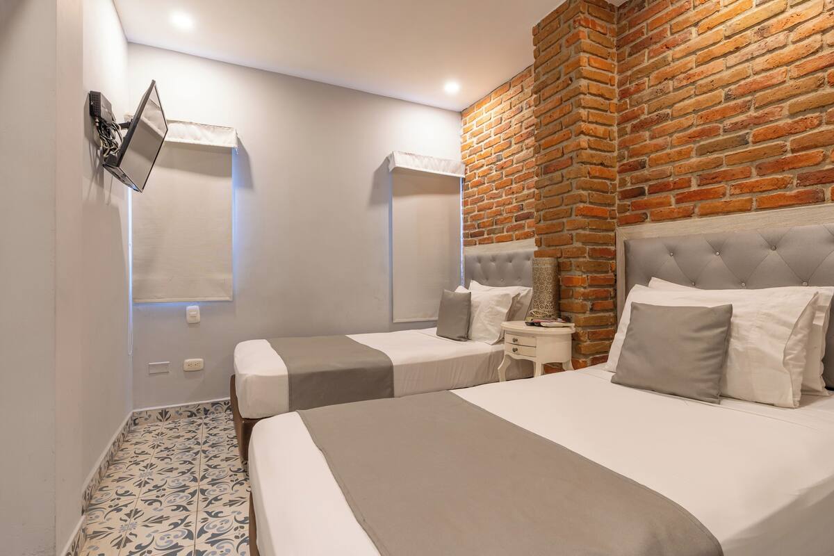 Una habitación de hotel moderna con una pared de ladrillo decorativa, dos camas, un televisor de pantalla plana montado en la pared y un piso con diseño.