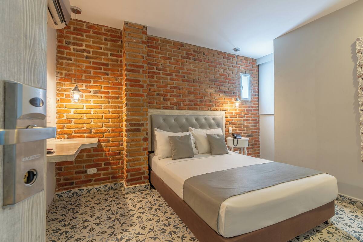 Un dormitorio con pared de ladrillo, cabecera capitonada, mesita de noche y baldosas de suelo estampadas.