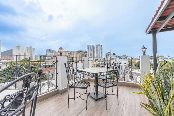 A balcony with a table and chairs, overlooking a cityscape with buildings and a mountain. - Hotel Boutique Adaz (Santa Marta)