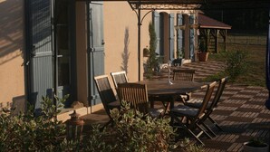 Un patio al aire libre con mesa y sillas de madera, una pérgola y un área de estar techada.