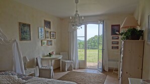Un dormitorio con cama, escritorio, sillón, araña y vistas al exterior.