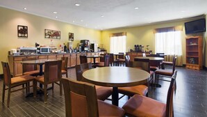 Un comedor de hotel con varias mesas y sillas, una estación de café y un televisor montado en la pared.