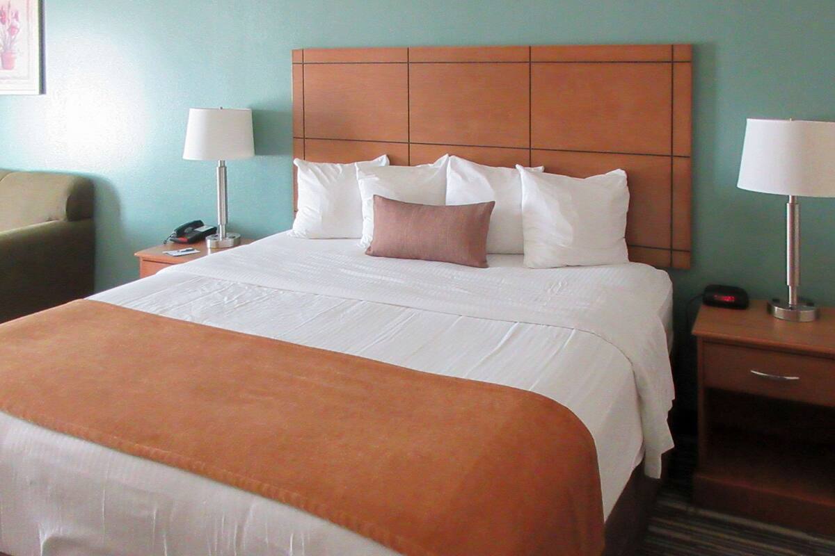 A hotel room with a large bed, a headboard, two bedside tables with lamps, and a chair.