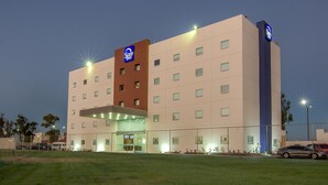 Un hotel de varios pisos con un letrero llamativo, un techo plano y una entrada bien iluminada.