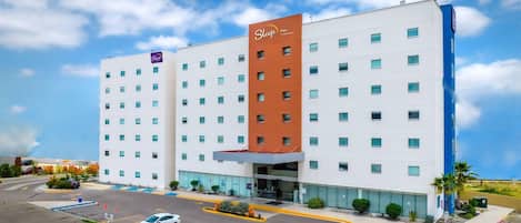 A Sleep Inn hotel with a modern design, featuring a prominent red and white color scheme, multiple floors, and a parking lot with several cars.