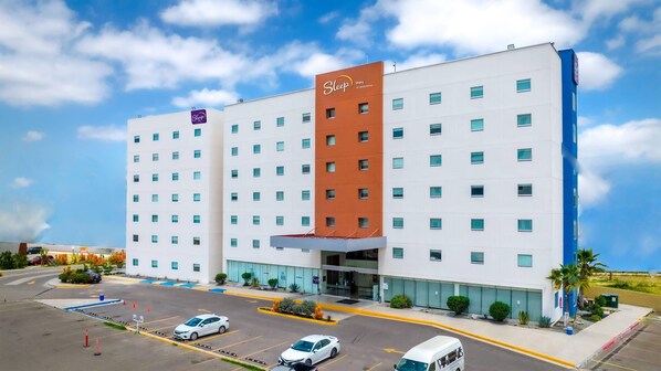 A Sleep Inn hotel with a modern design, featuring a prominent red and white color scheme, multiple floors, and a parking lot with several cars.