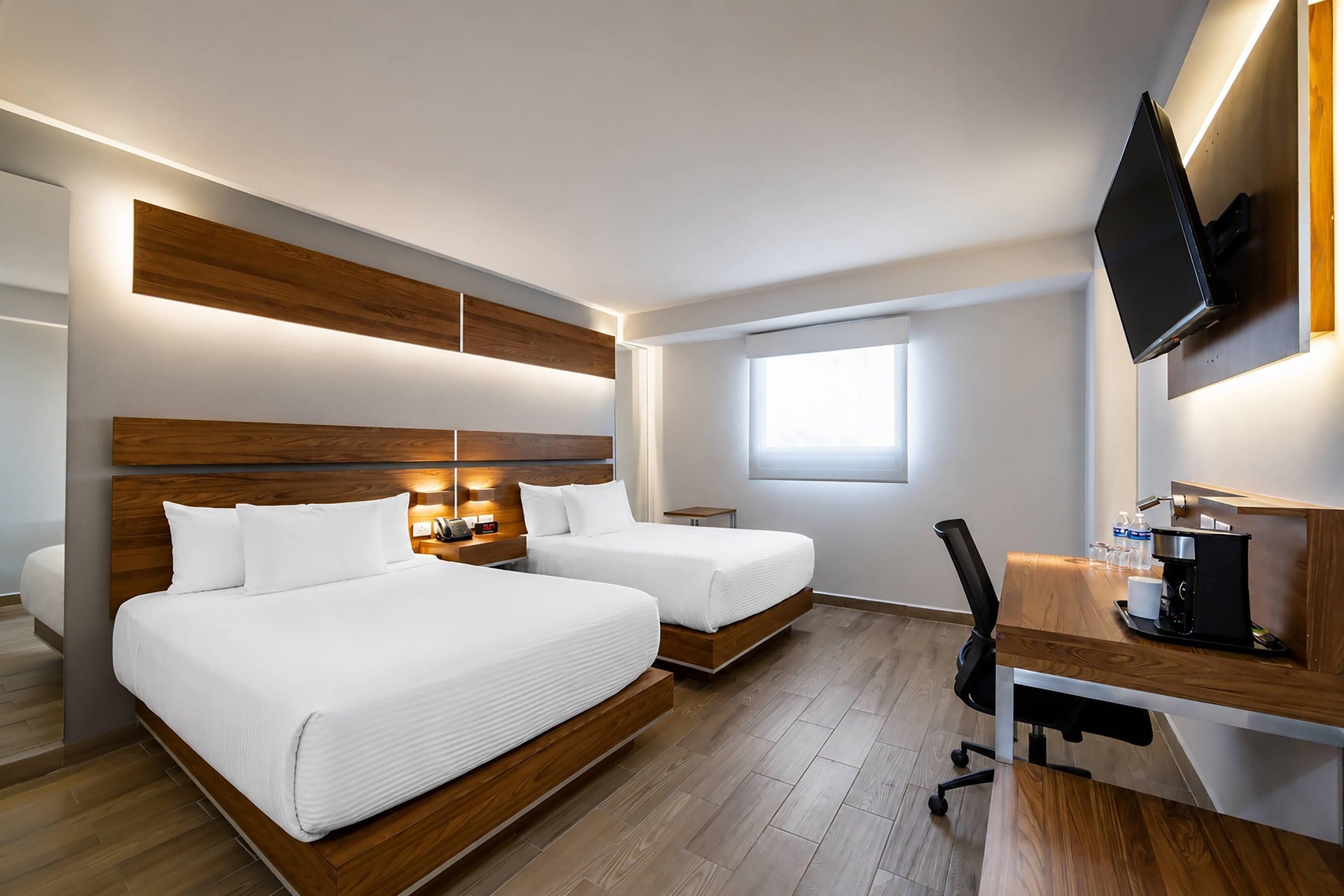 Habitación de hotel con dos camas, un escritorio con cafetera, un televisor y una ventana.