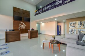 A modern hotel lobby with a reception desk, a seating area with a sofa and coffee table, and artwork on the walls.