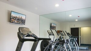 Un gimnasio con cintas de correr, un espejo grande y una pintura de un paisaje urbano.