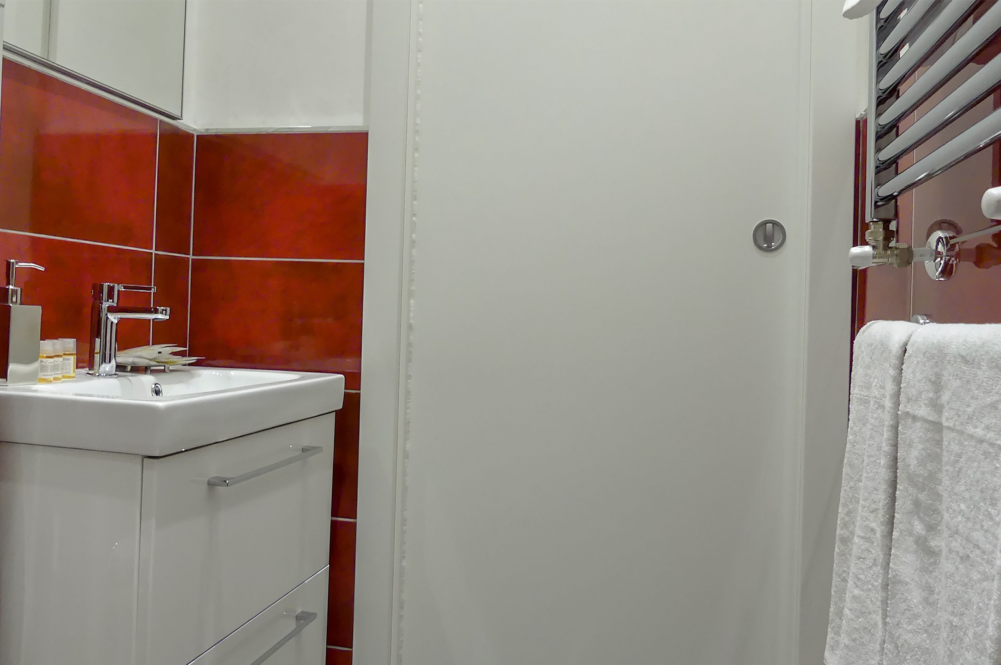 Un baño con un lavamanos blanco, baldosas rojas, un perchero y una puerta.