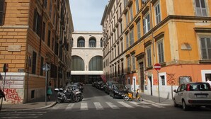 Un carrer amb cotxes i motocicletes aparcades, edificis amb finestres apuntades, i un cel serè.