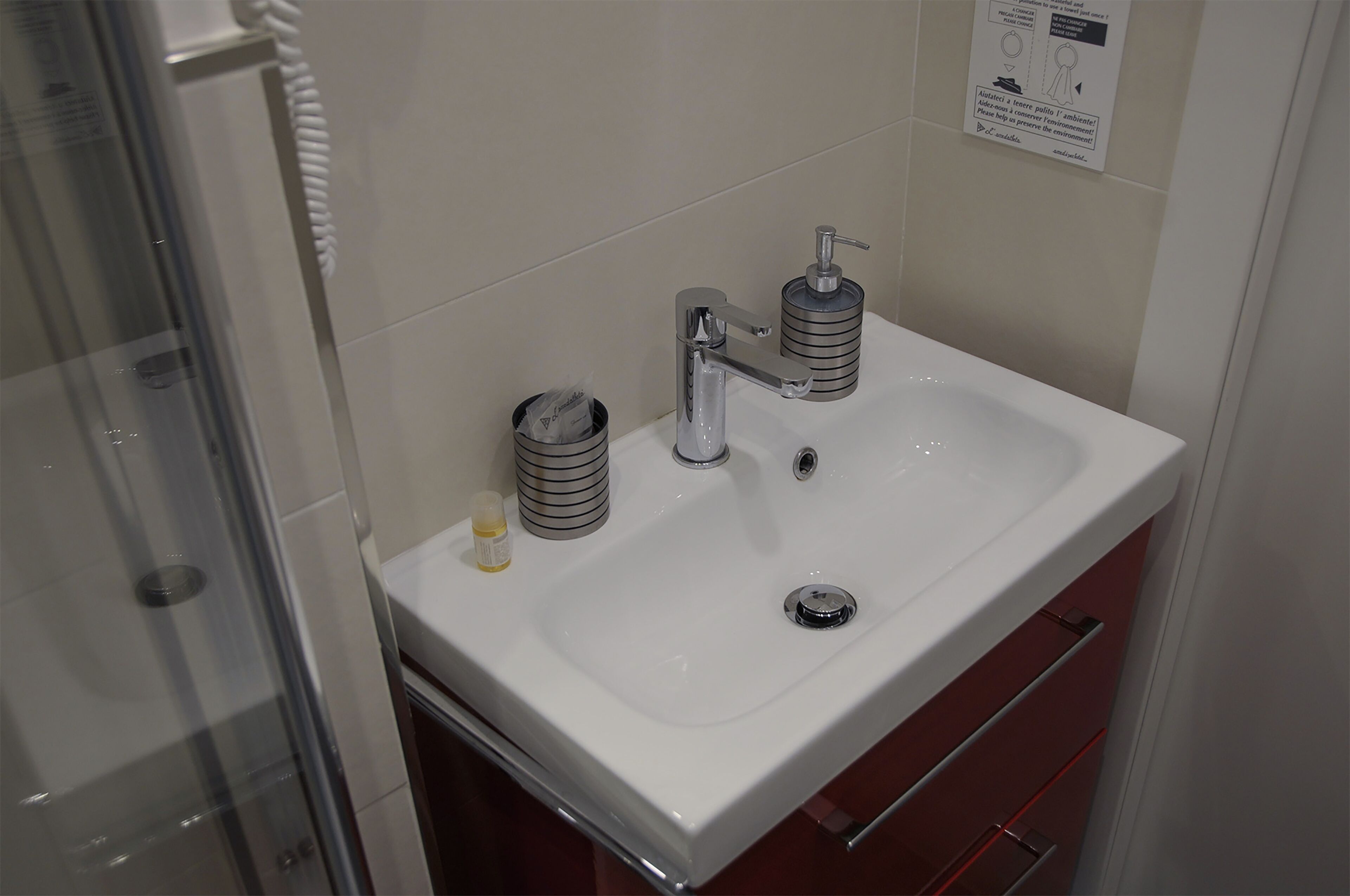 A bathroom with a white sink, two soap dispensers, a glass shower enclosure, and a red cabinet.