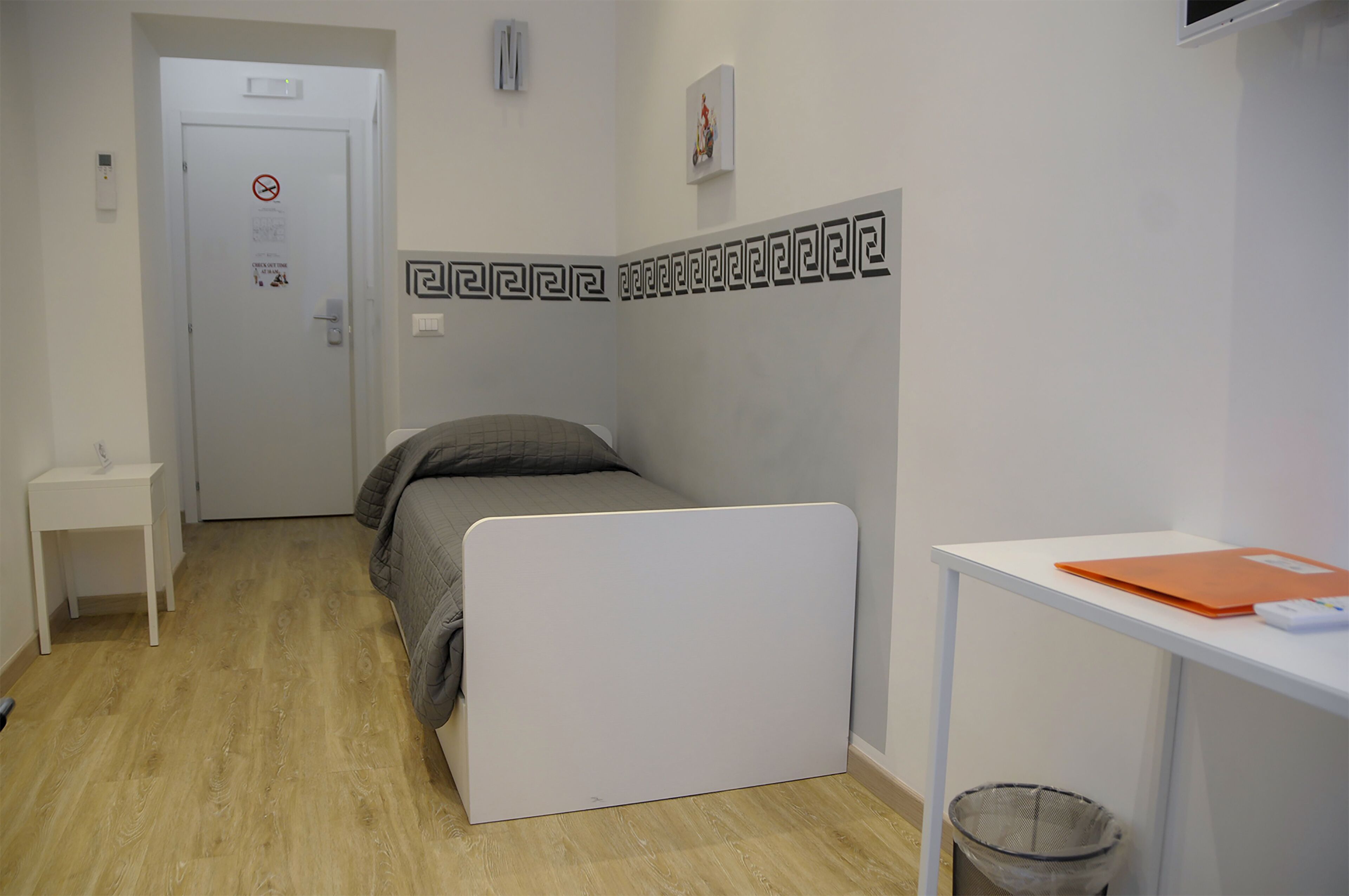 Una habitación pequeña y ordenada con una cama, un escritorio y un cubo de basura.