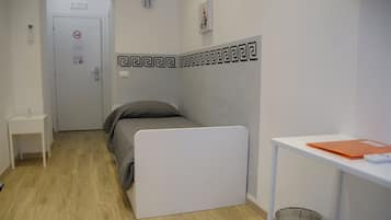 A small, neatly arranged room with a bed, a desk, and a trash bin.