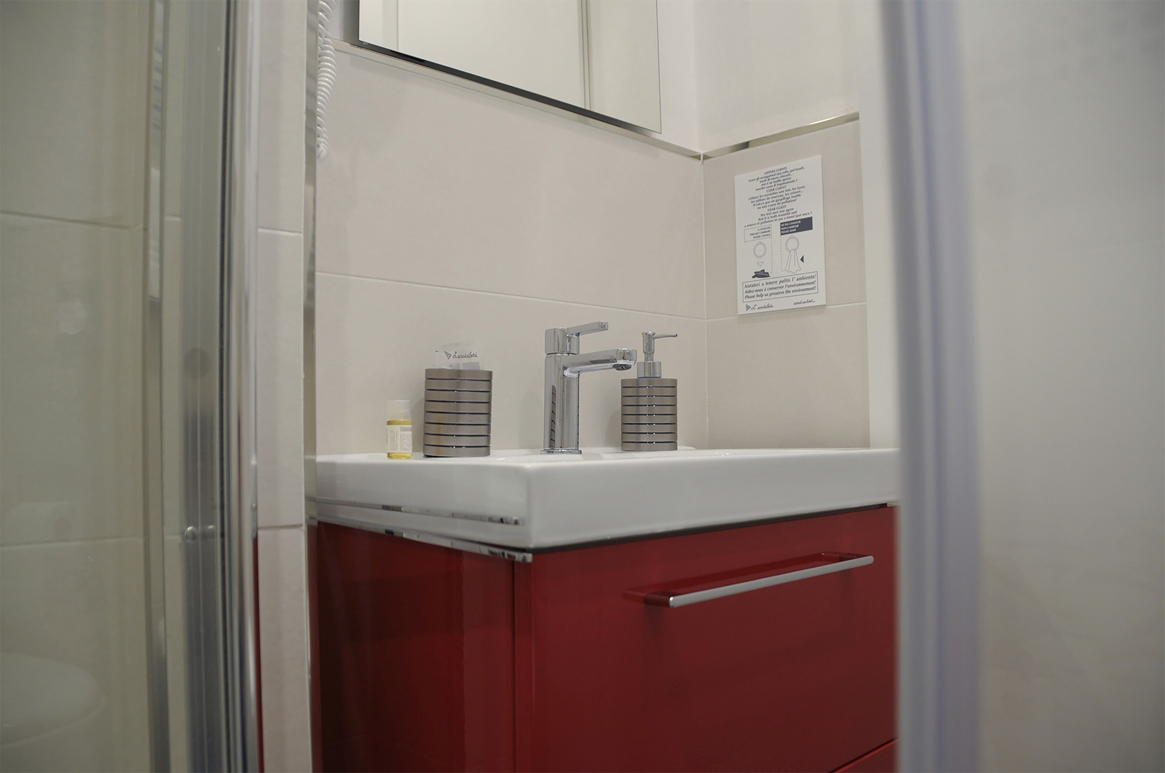 Un bagno con un lavandino bianco, mobili rossi e box doccia in vetro.