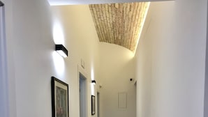 Passadís estret amb parets blanques, sòl de fusta i sostre amb un dibuix relleuat.
