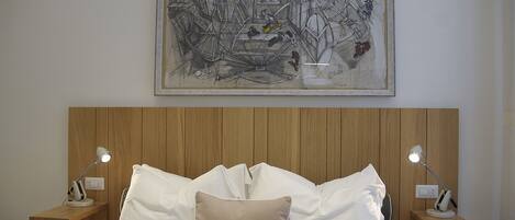 A neatly made bed with white and beige pillows, two bedside tables with lamps, and a large framed abstract artwork above the bed.