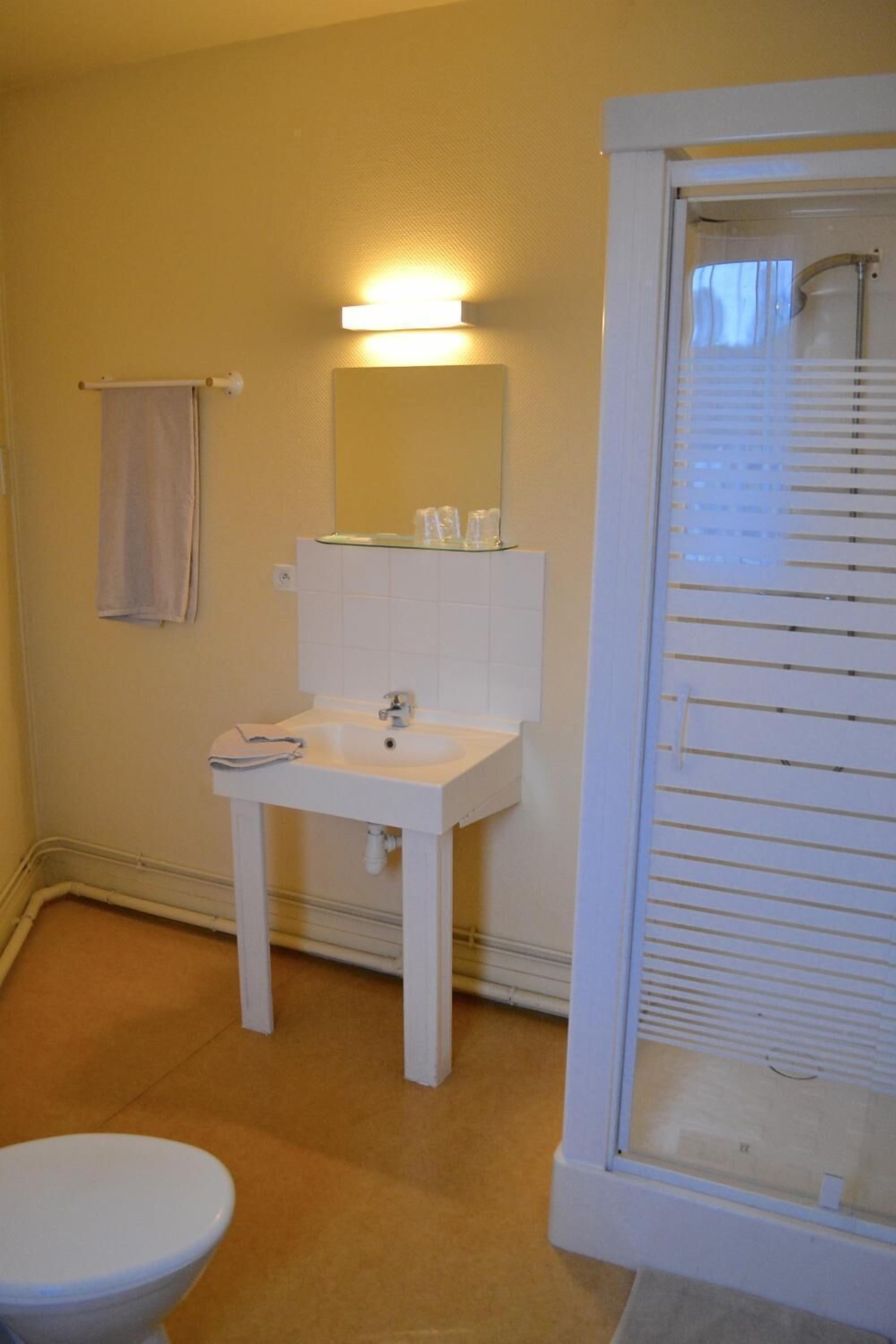 A bathroom with a white sink, mirror, and toilet. There is a towel hanging on a rack and a window with blinds.