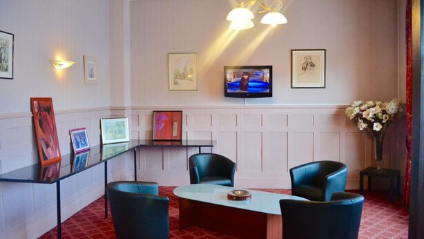 A hotel room with a round table, four chairs, a flat-screen TV mounted on the wall, and framed artwork on the walls.