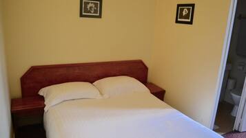 A single bed with a wooden headboard and white bedding in a room with plain walls.