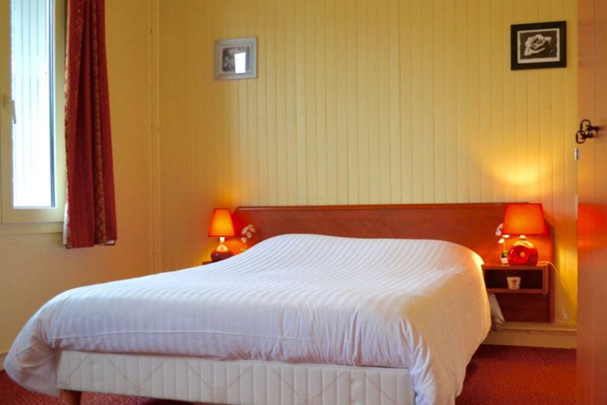 Hotellihuone, jossa on suuri sänky, kaksi yöpöytävalaisinta, puinen sängynpääty ja ikkuna, jossa on verhot.