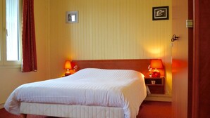 A hotel room with a large bed, two bedside lamps, a wooden headboard, and a window with curtains.