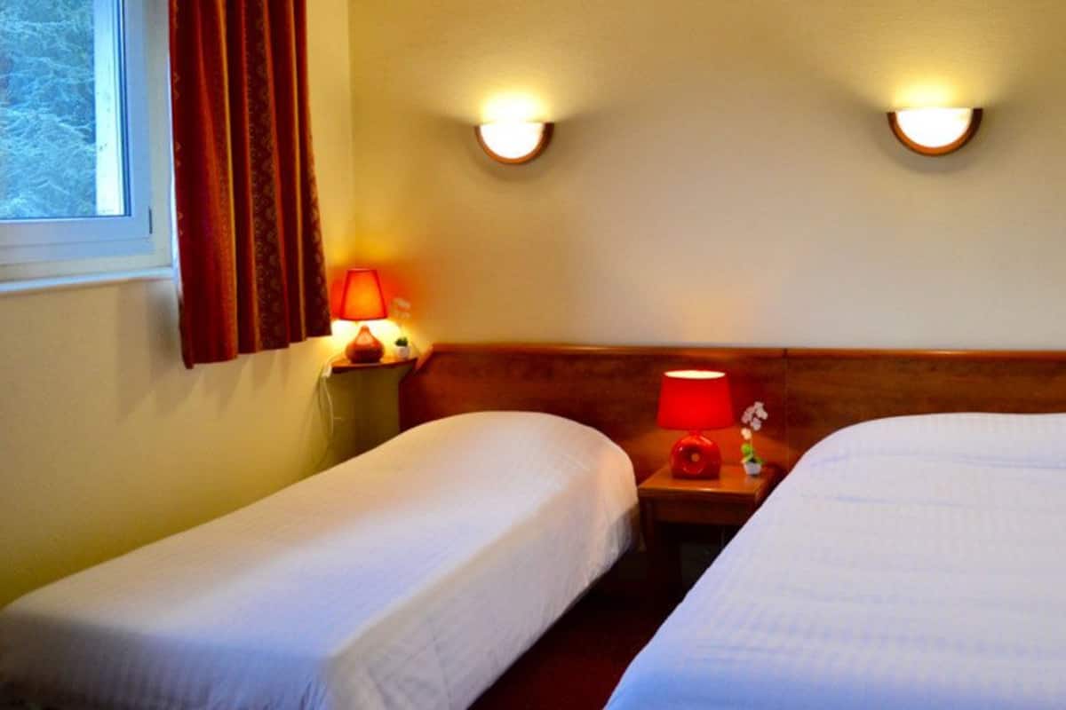 Hotellihuone, jossa on kaksi erillistä sänkyä, yöpöytä lampun kanssa ja seinään kiinnitetyt valaisimet.