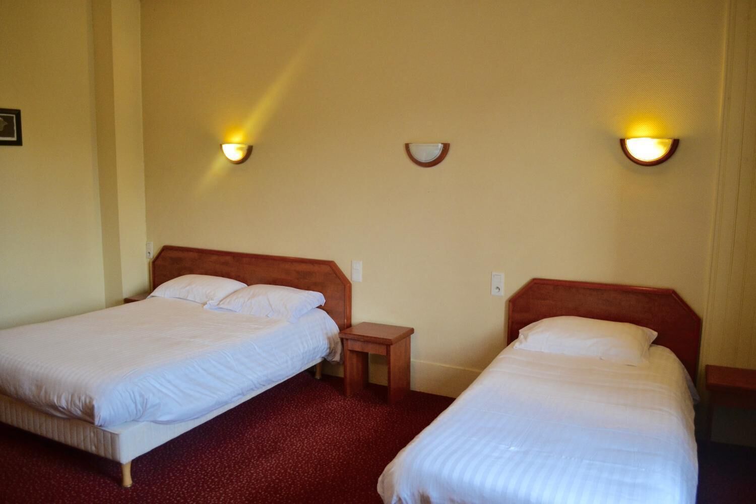 A hotel room with two single beds, a small bedside table, and wall-mounted light fixtures.